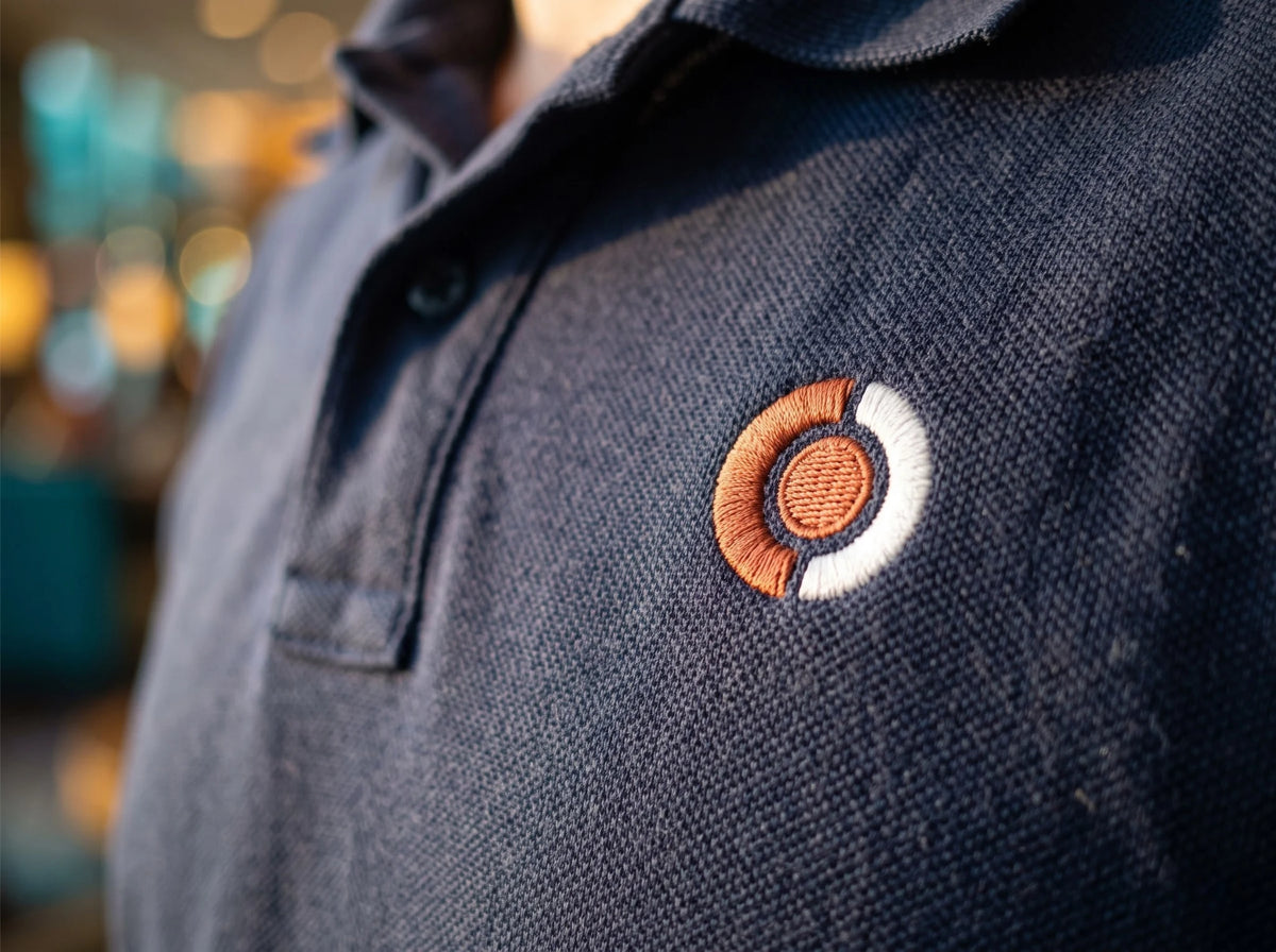 Close-up of a navy custom embroidered polo shirt with a stitched company logo on the left chest